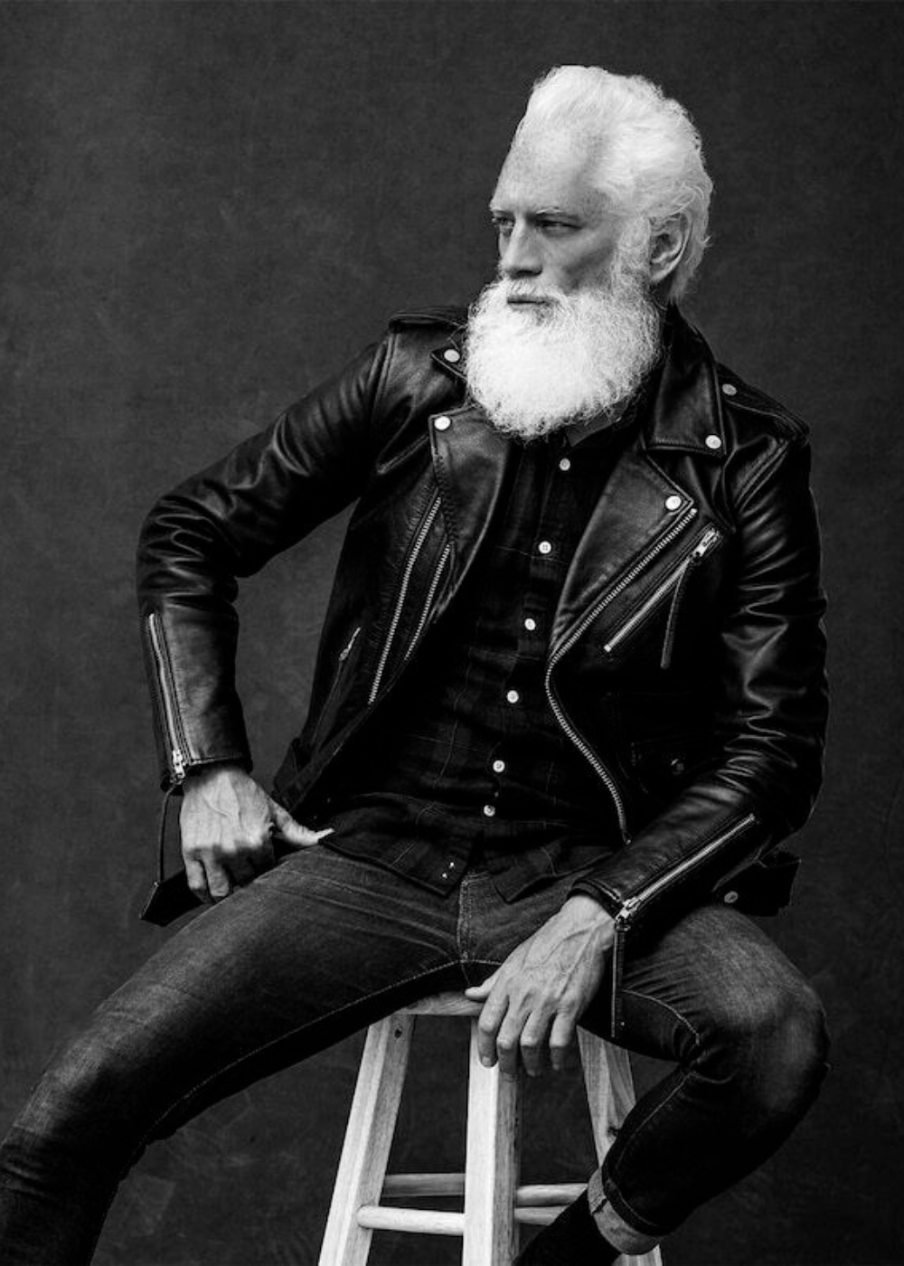 Black leather biker jacket on model sitting on stool – stylish men’s motorcycle jacket.