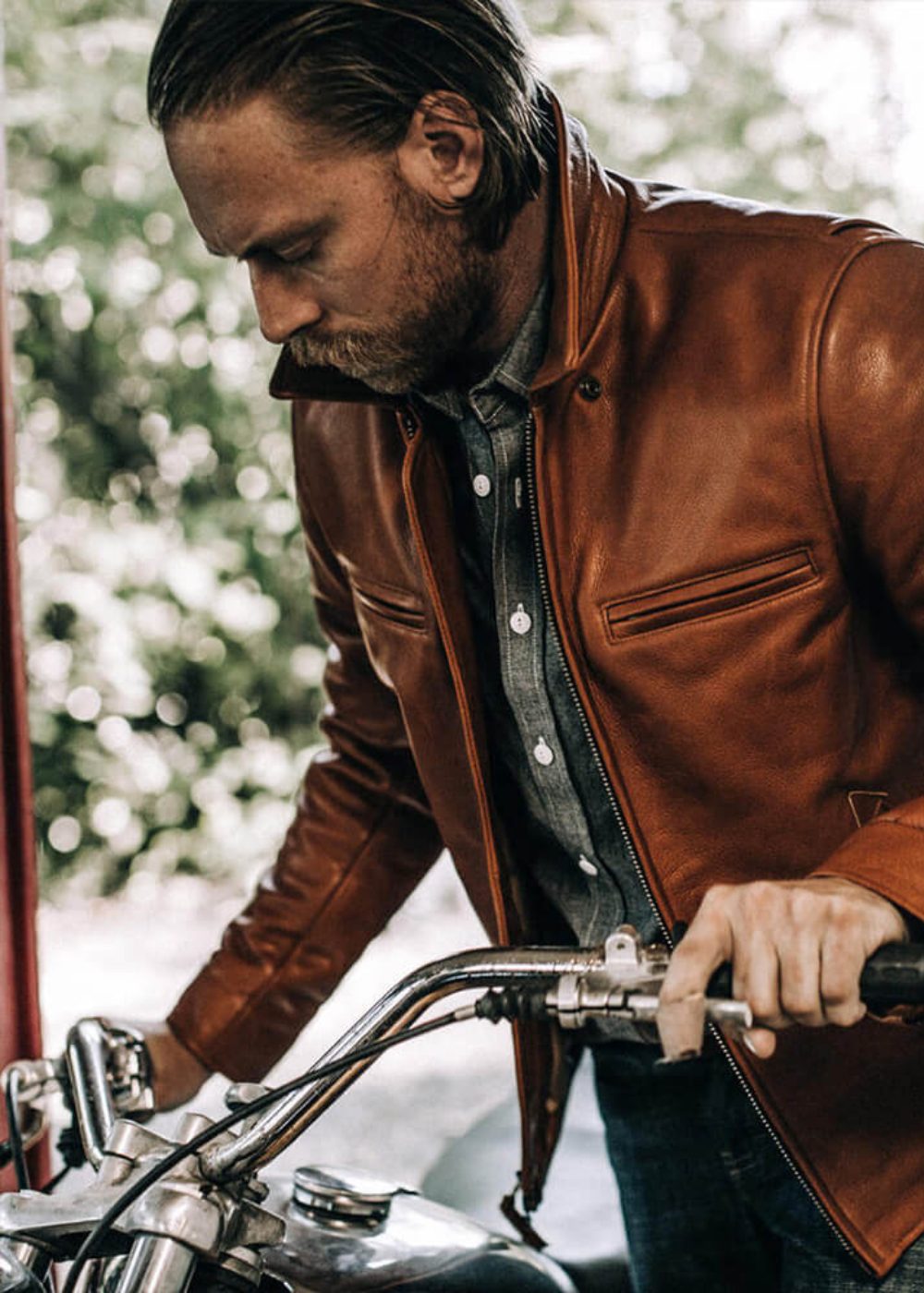 Man wearing a brown leather motorcycle jacket while riding a bike, showcasing the jacket's premium design and biker style.