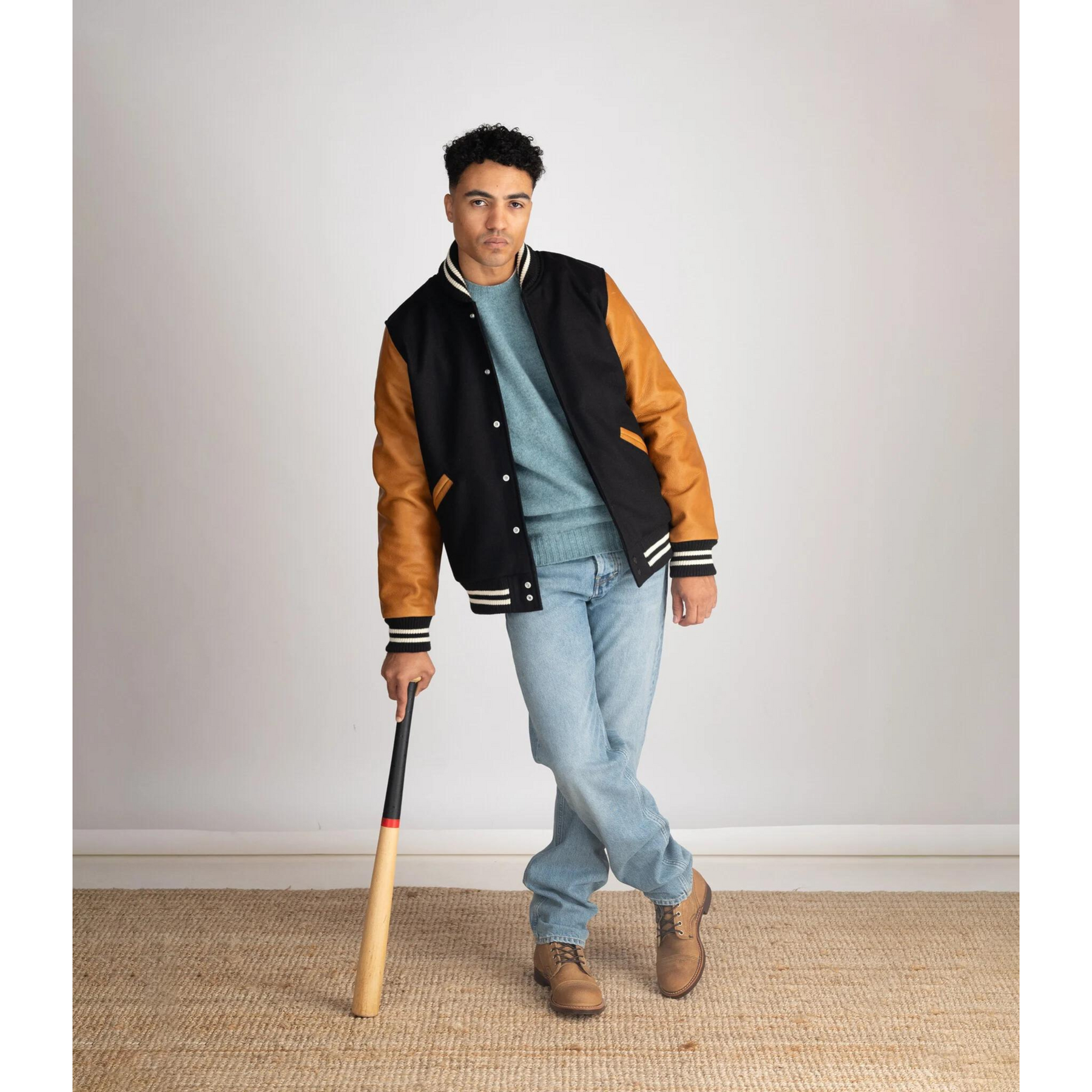 Full-body shot of a model holding a baseball bat, wearing the Black Varsity Jacket with Brown Leather Sleeves – emphasizing casual athletic style.